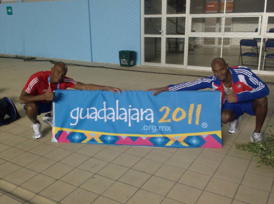 Giraldo y Raydel Carales posan para una foto junto a un cartel identificativo de los Juegos Panamericanos de Guadalajara 2011