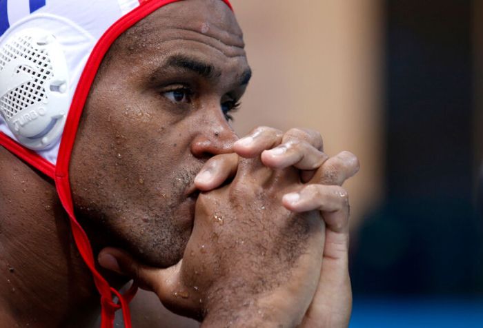 El polista cubano Iván Pérez de perfil con gorro blanco y rojo observa pensativo con los dedos cruzados a la altura de la boca y la nariz.