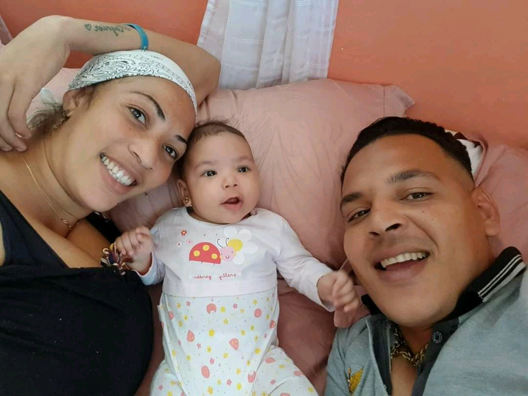 Arismey Ramos (izquierda) junto a su hija Ahytana (centro) y su esposo Mas Castro (derecha) sonríen sobre la cama para una foto selfie.